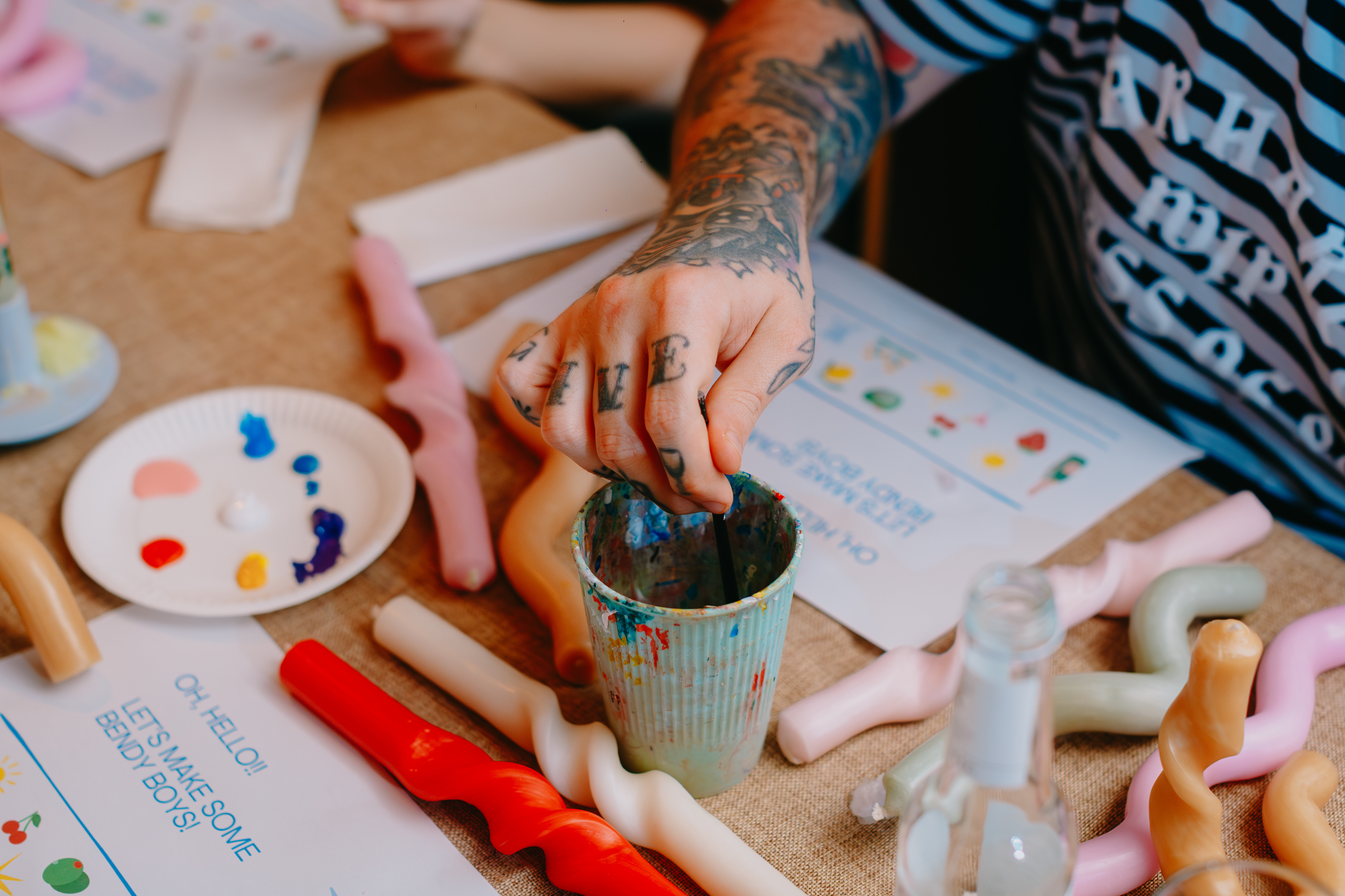 Man's tattooed hand dipping a paintbrush into a cup